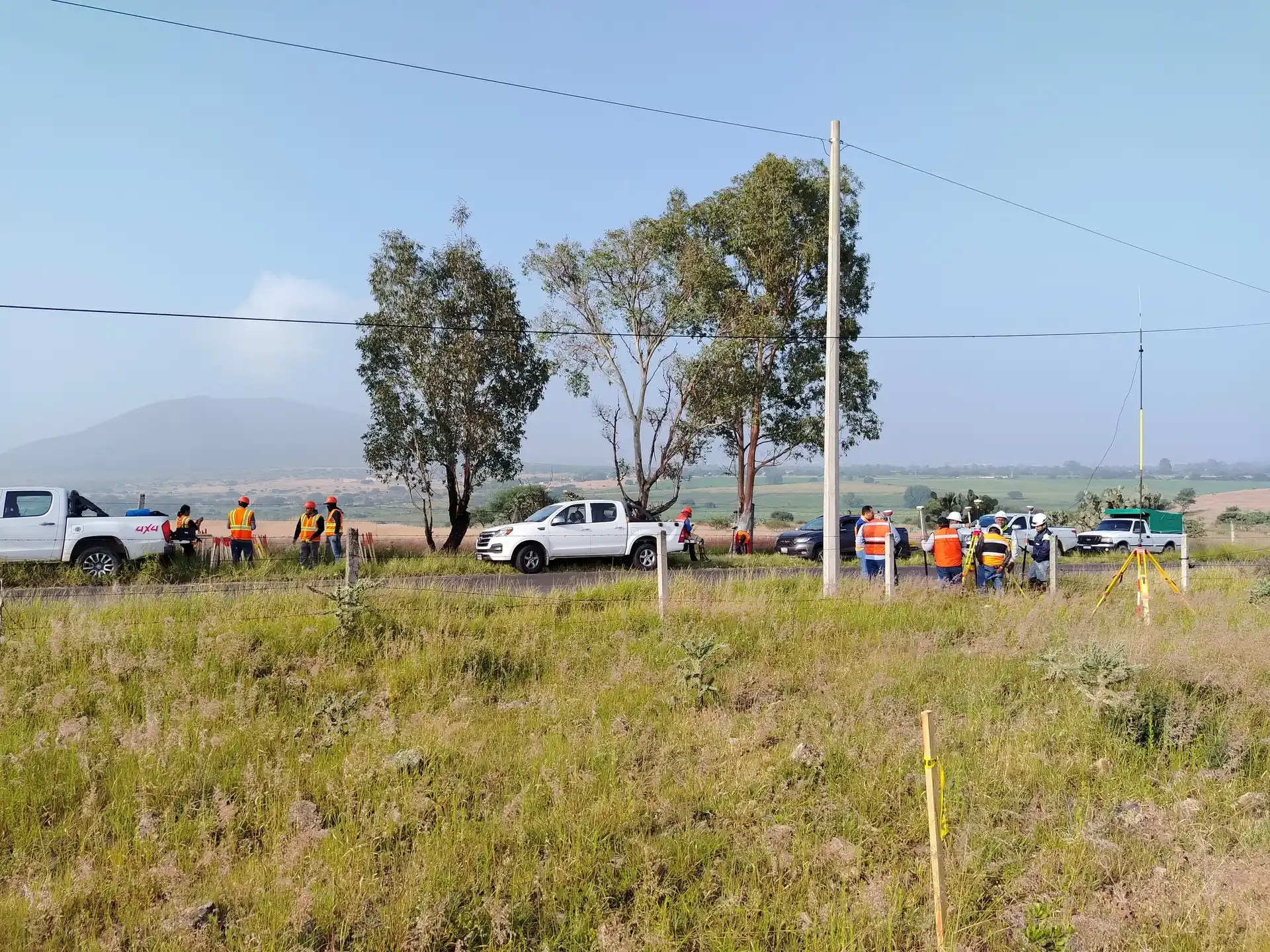 Brigada de topografía con GNSS junto a un camino y postes