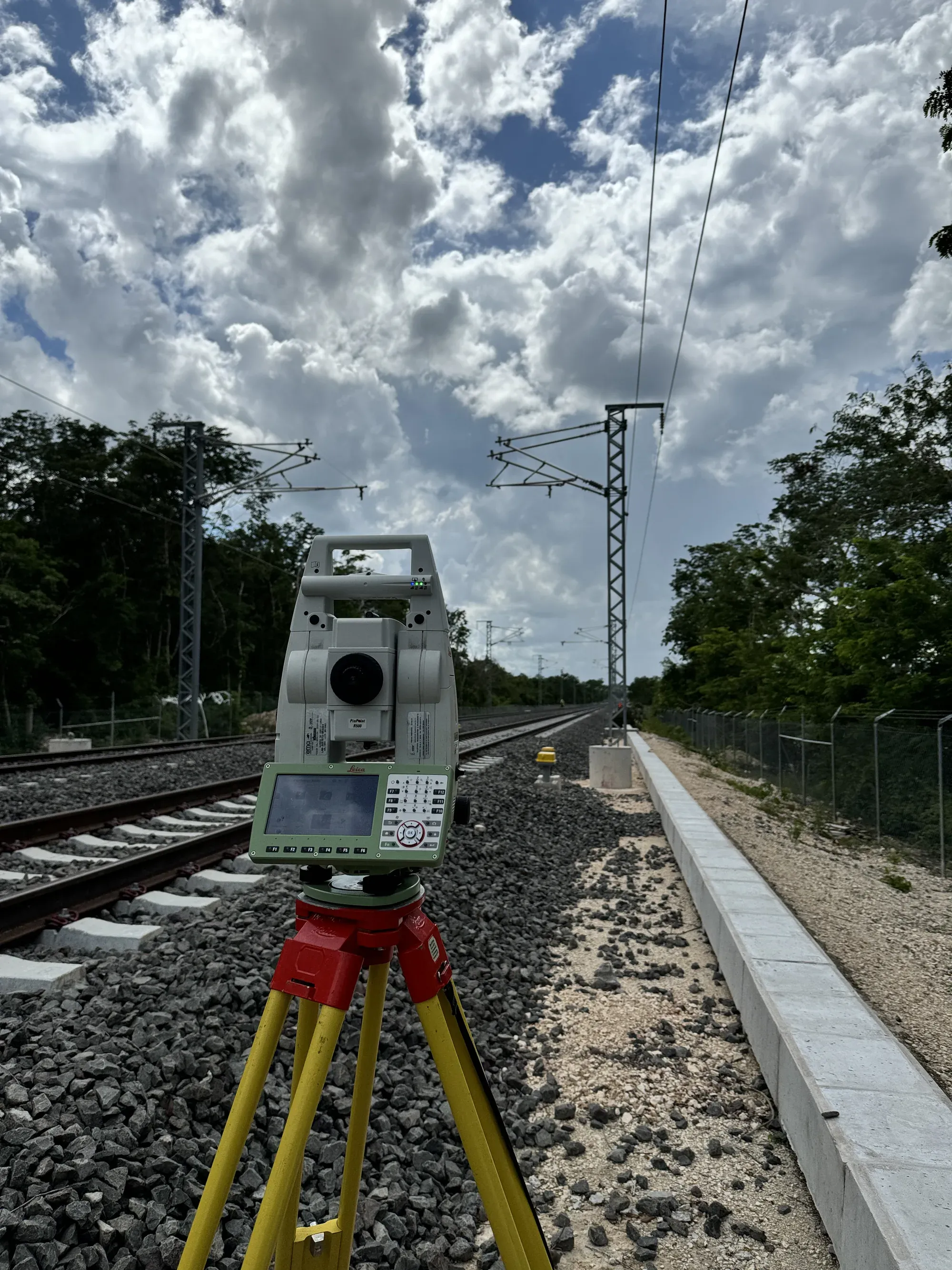 Estación total en primer plano sobre la vía con catenaria