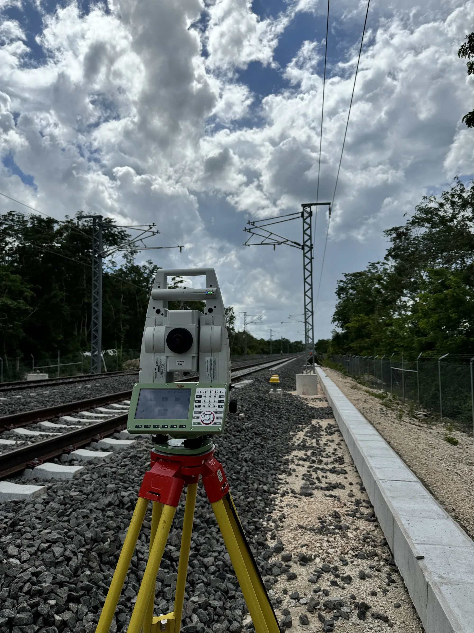 Estación total sobre tripié junto a vía electrificada