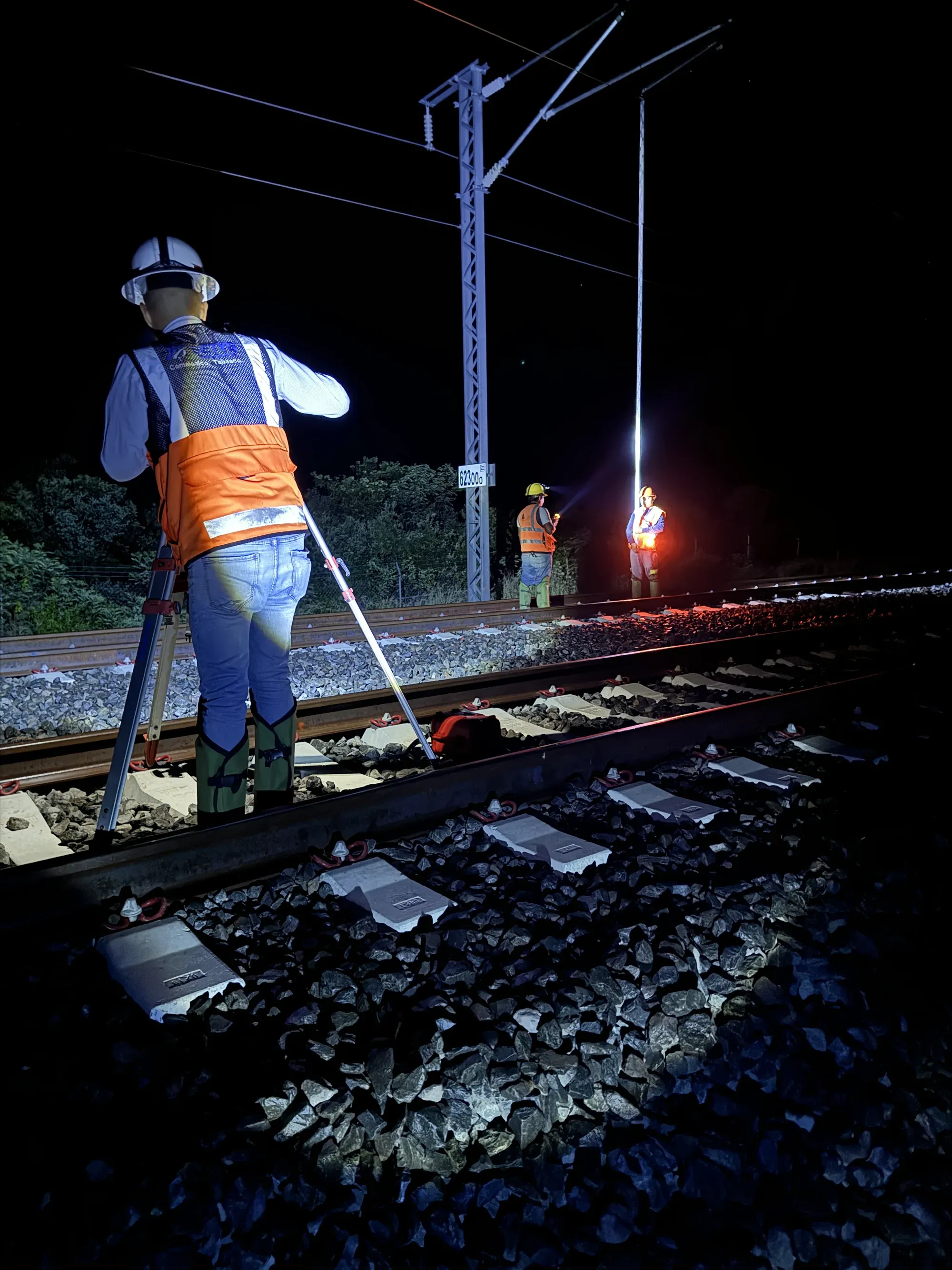 Mira de nivelación sobre la vía de noche, con catenaria iluminada