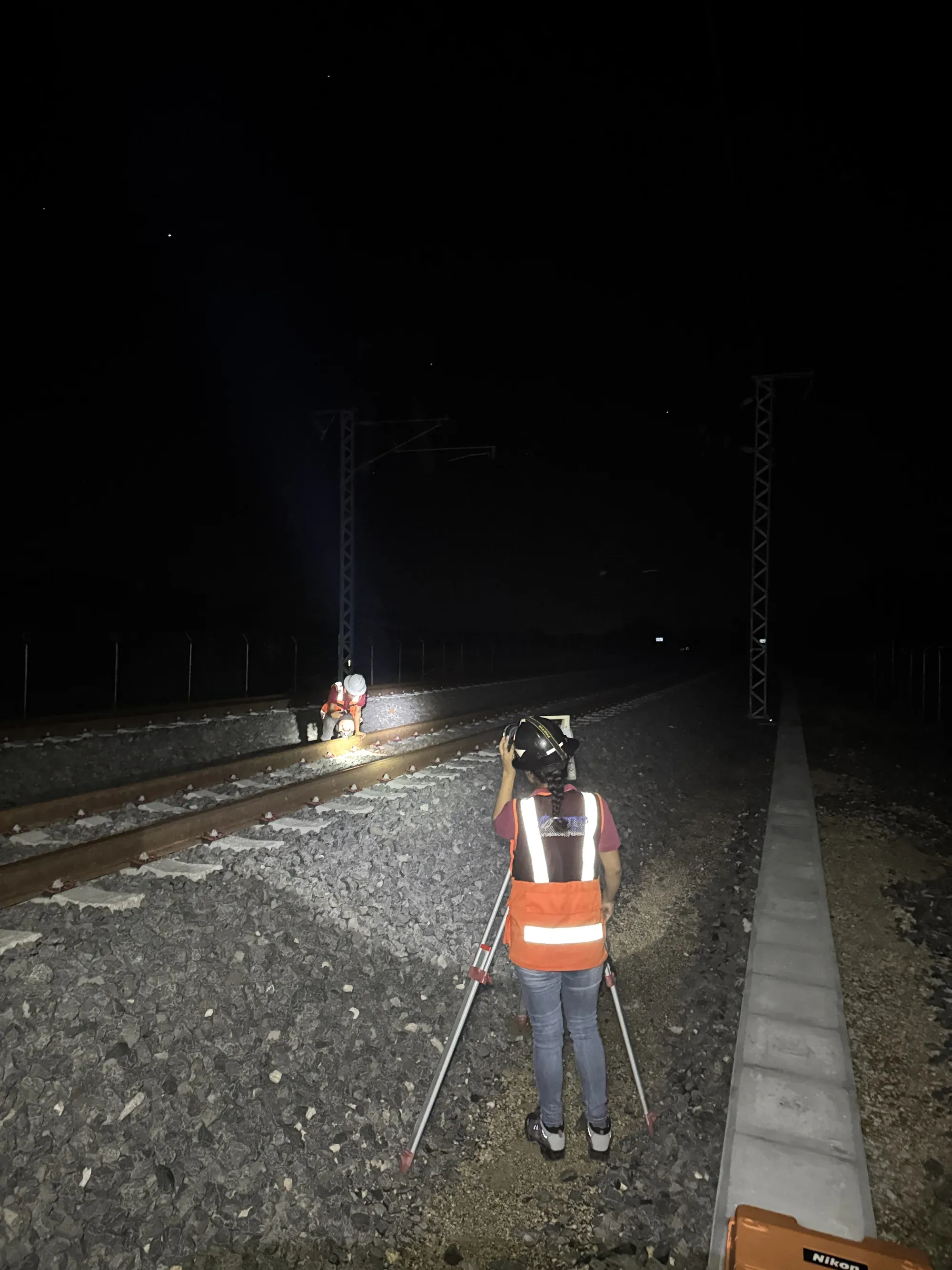 Topógrafo de espaldas con lámpara frontal sobre la vía, de noche