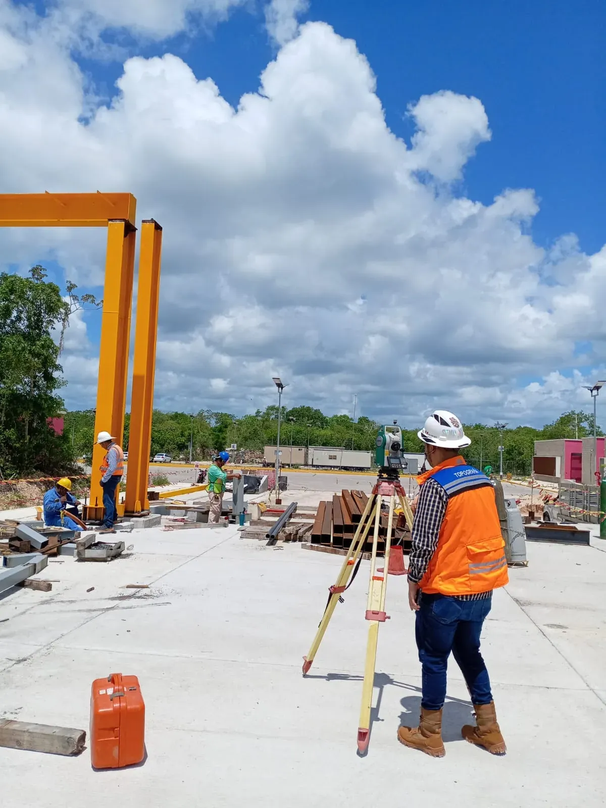 Topógrafo de espaldas con estación total bajo pórtico amarillo del taller