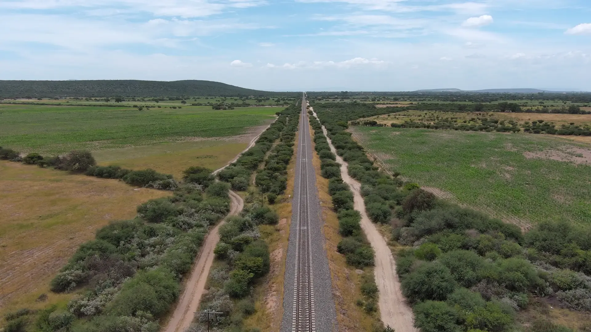 Vía férrea entre parcelas verdes vista desde dron