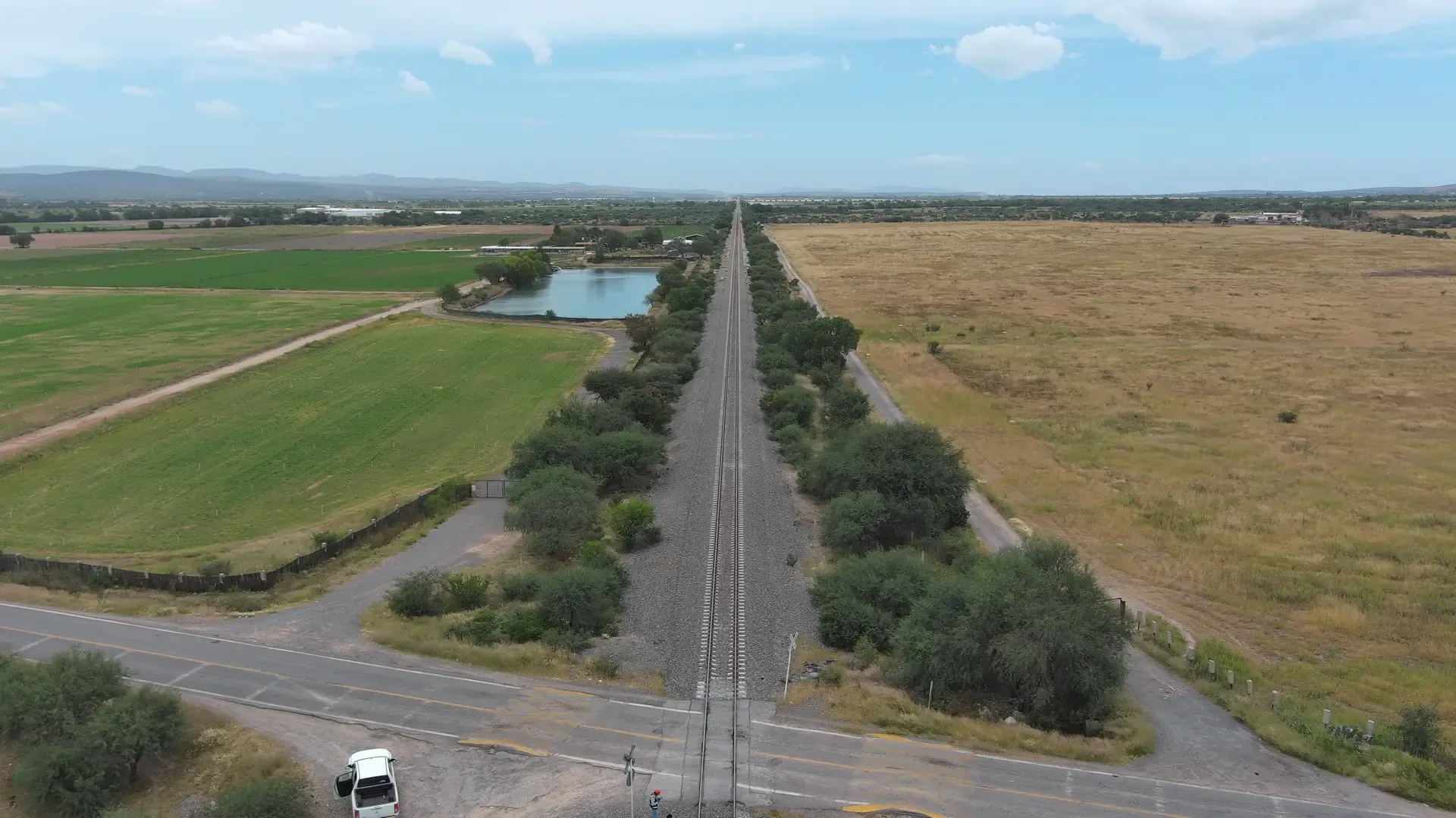 Vía férrea vista desde dron junto a un bordo de agua y parcelas